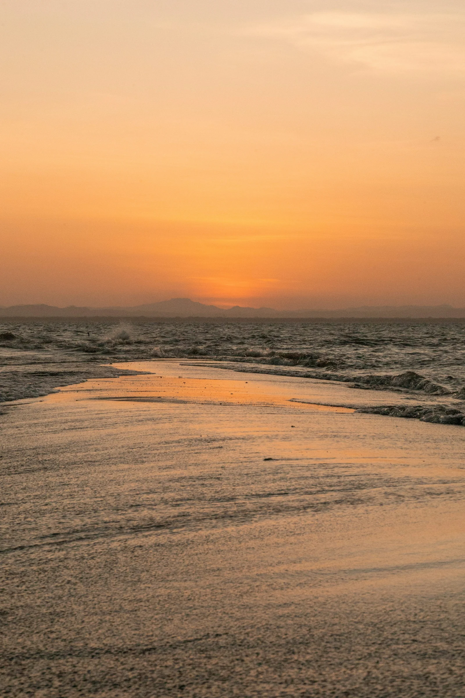 Waves meet a strip of sand at Punta Jesús María beneath an orange sunset sky